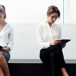 Zwei Frauen sitzen in einem Wartezimmer an Tablets